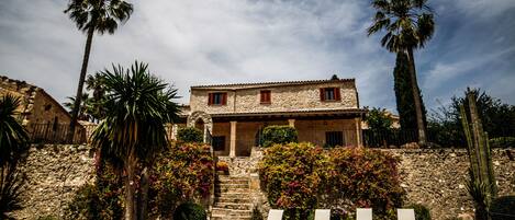 A stone house with a terrace, palm trees, and a stone wall.