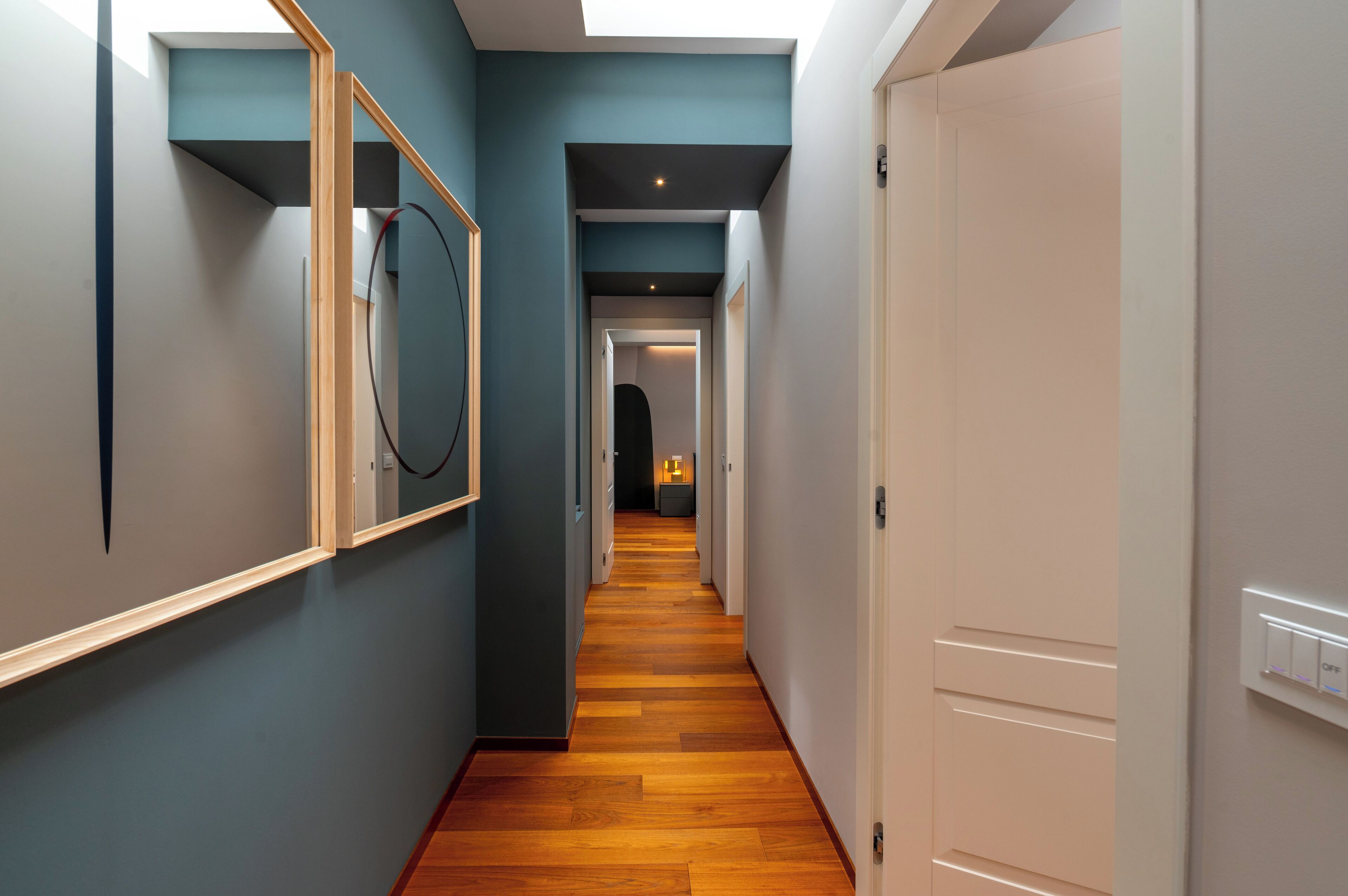 A modern hallway with wooden flooring, a large mirror, and a door with a light switch.