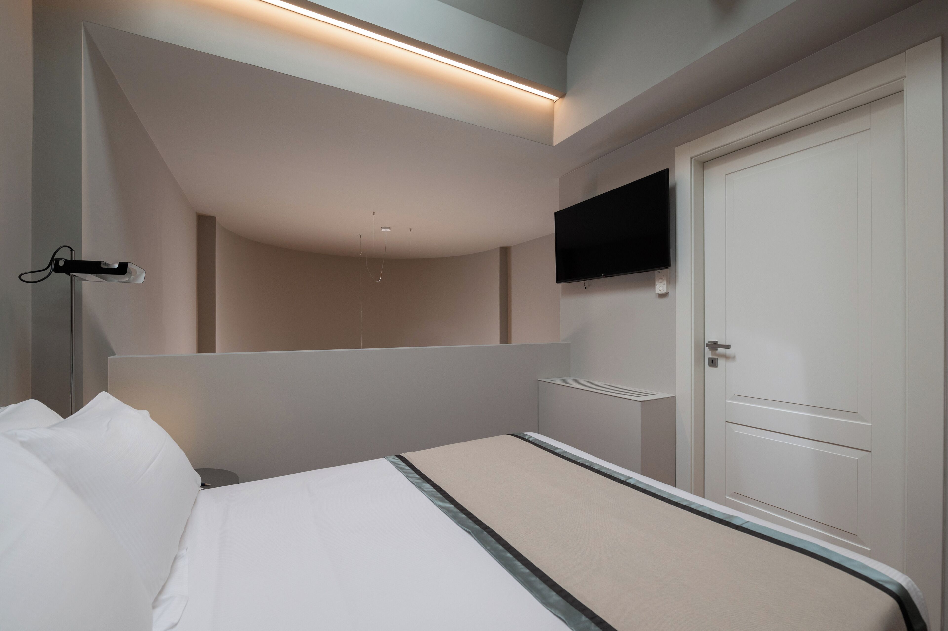 Et moderne hotelværelse med en seng, et fladskærms-TV ophængt på væggen og en dør med håndtag.