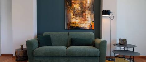Ein modernes Wohnzimmer mit einem grünen Sofa, einem großen abstrakten Gemälde an der Wand, einer Stehlampe und einem kleinen Tisch mit einem Telefon.