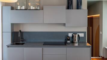A modern kitchen with grey cabinetry, a black countertop, a built-in sink, and a coffee maker.