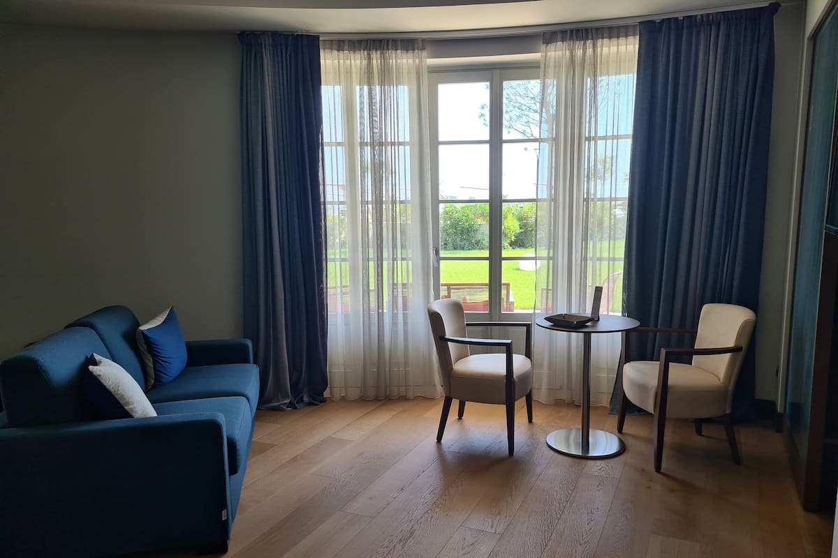 A living room with a blue sofa, two chairs, a small round table, and a large window with curtains.