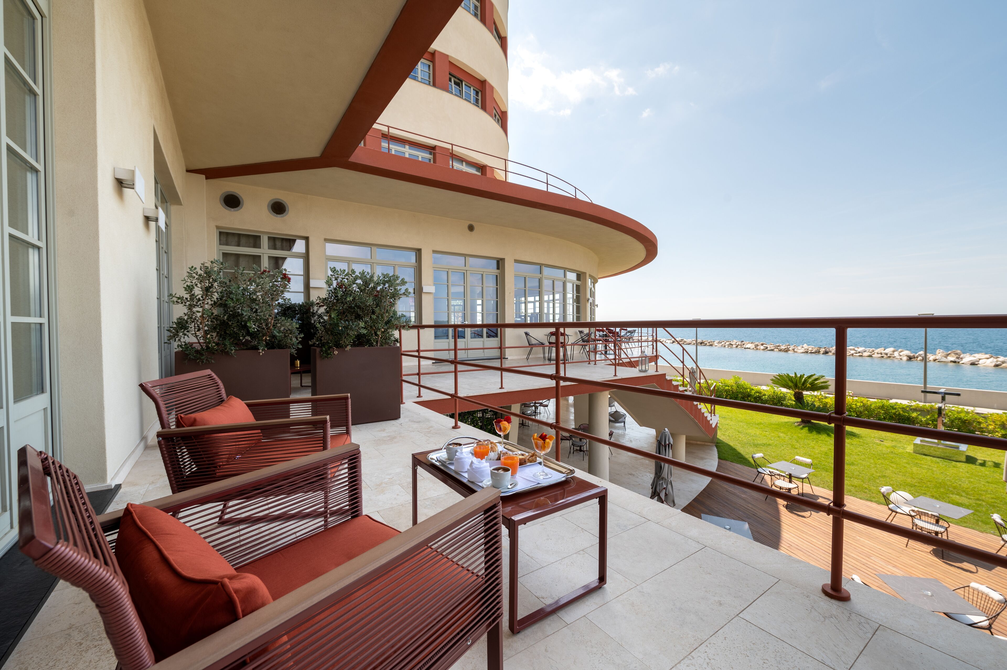 A balcony with wooden furniture, a dining table with breakfast items, and a view of the sea.