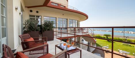 A balcony with wooden furniture, a dining table with breakfast items, and a view of the sea.