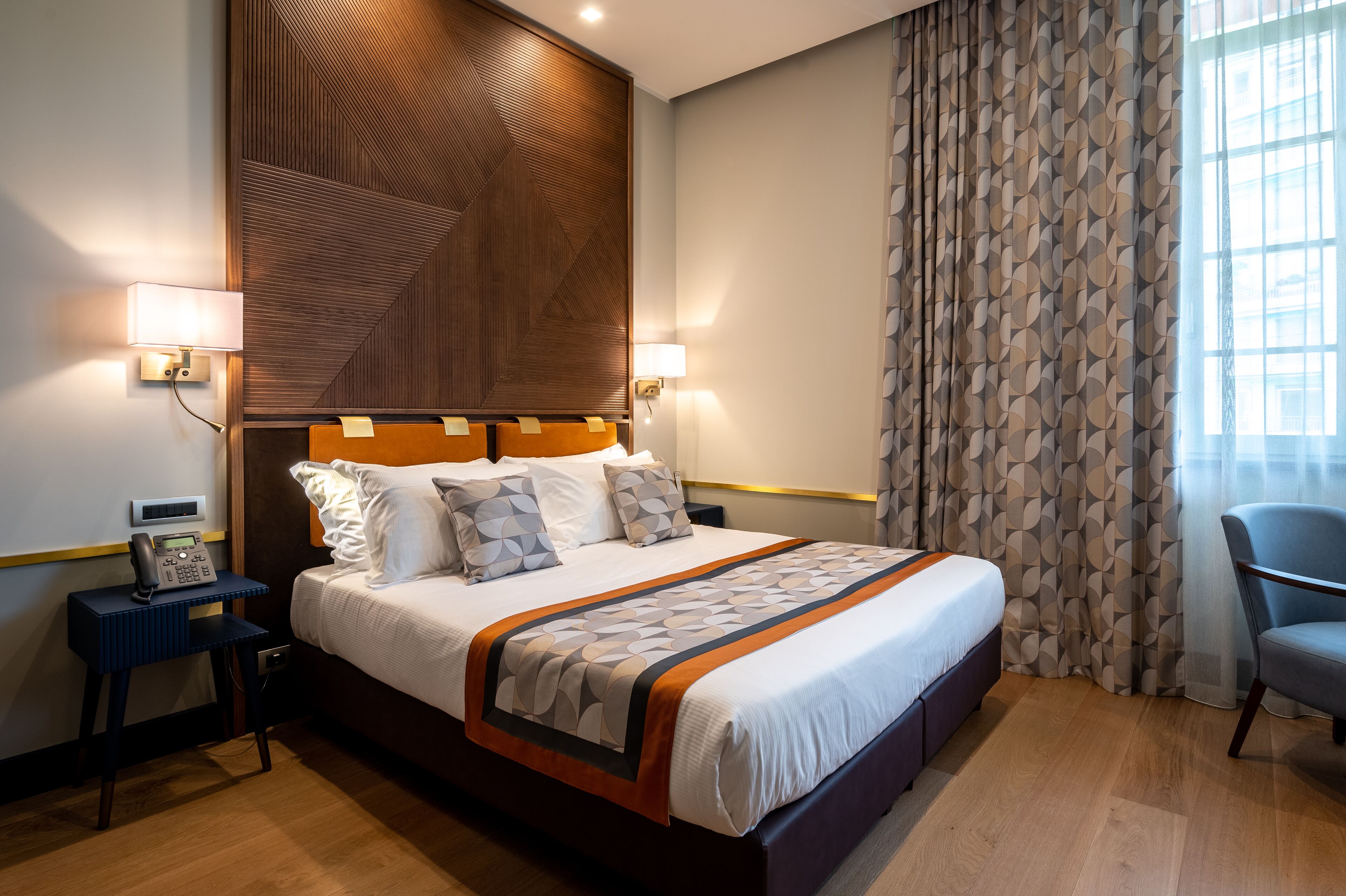 Habitación de hotel con una cama grande, lámparas de noche, un teléfono y una silla.