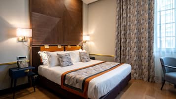 Habitación de hotel con una cama grande, lámparas de noche, un teléfono y una silla.