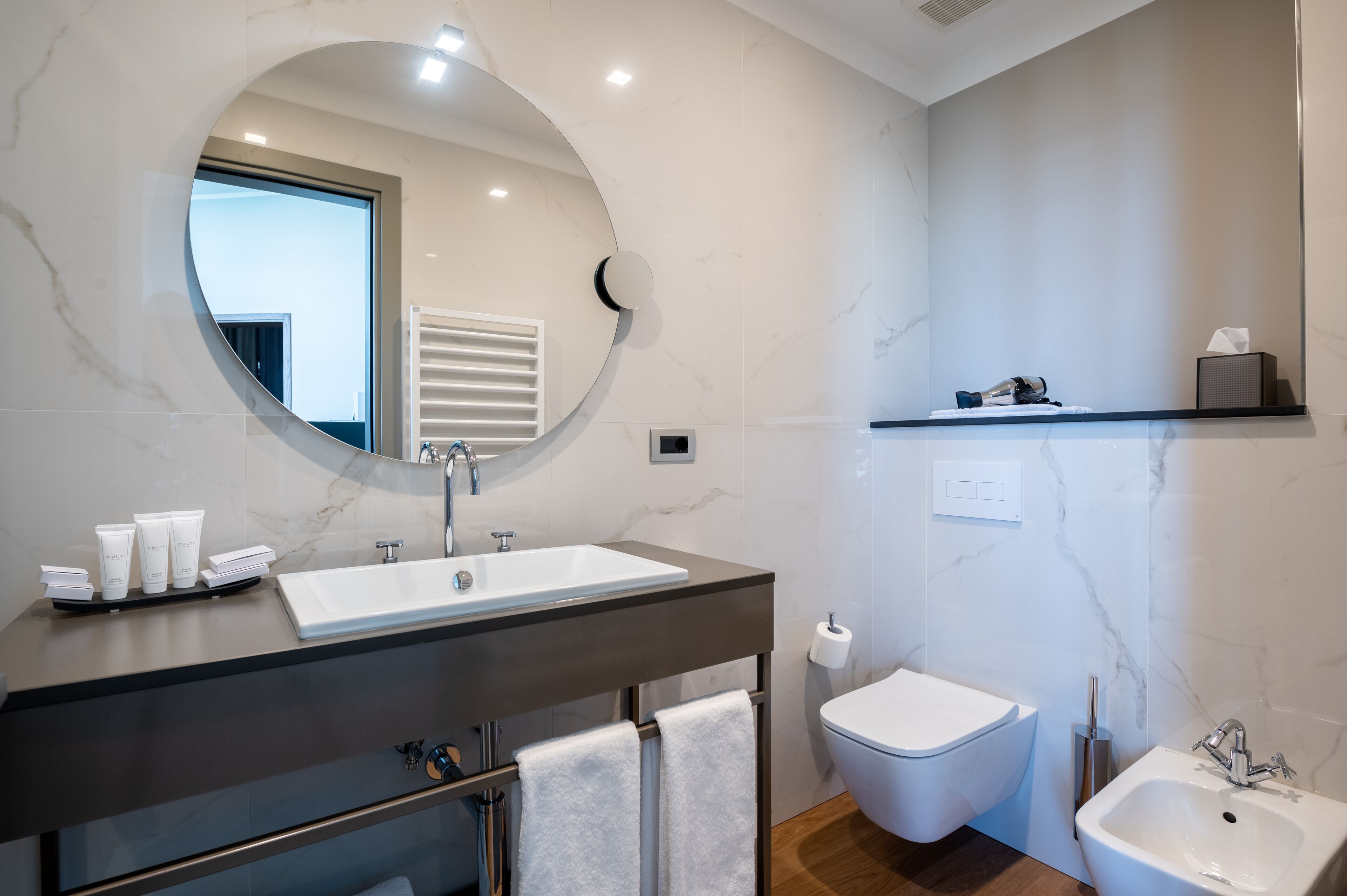 Ein modernes Badezimmer mit einem großen Spiegel, einem Waschbecken, einem Bidet und einer kleinen Ablage für Pflegeprodukte.
