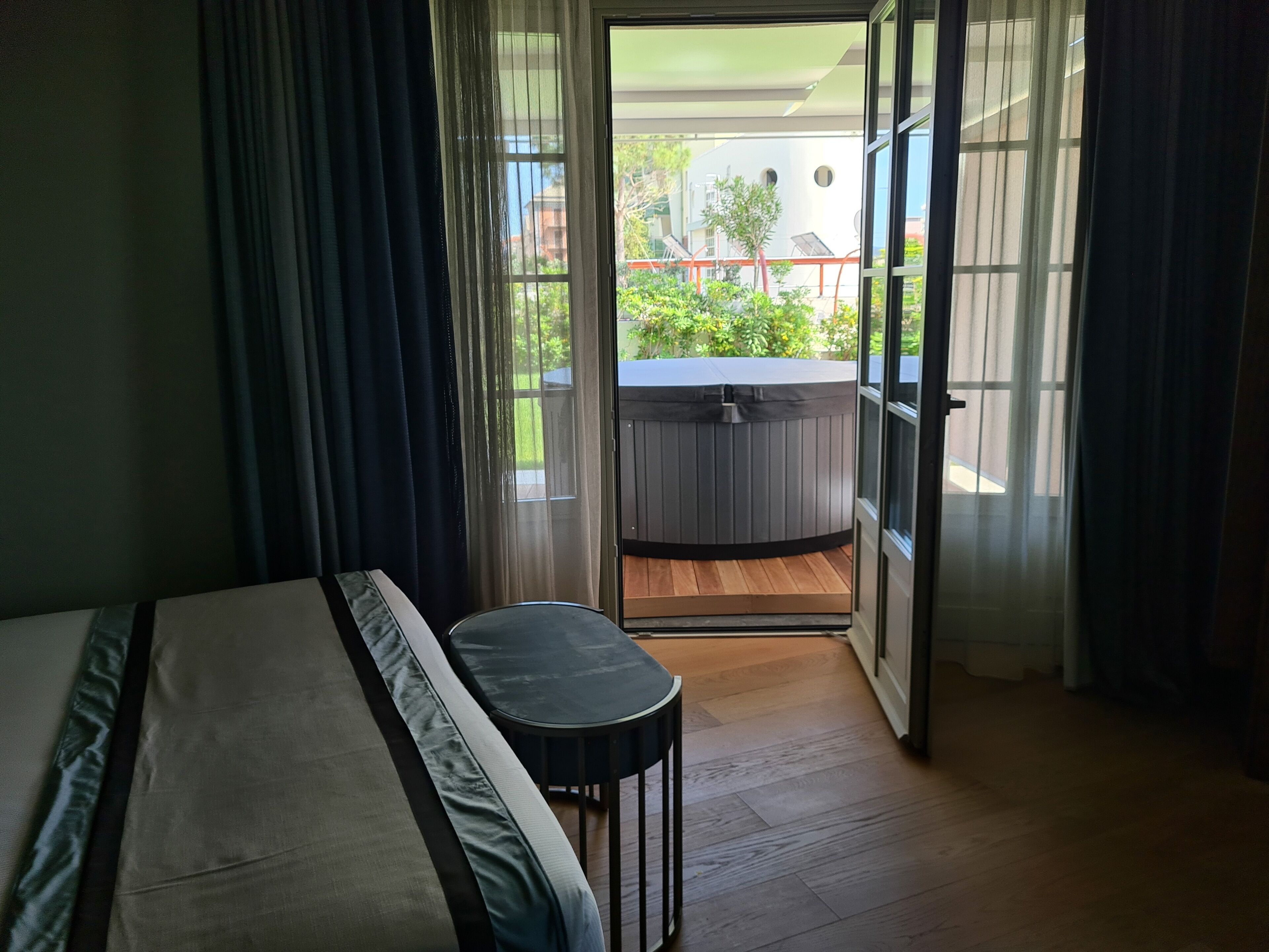 A room with a bed, a small table, and a view of a hot tub outside.