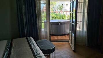 Ein Zimmer mit einem Bett, einem kleinen Tisch und Blick auf eine Whirlwanne draußen.