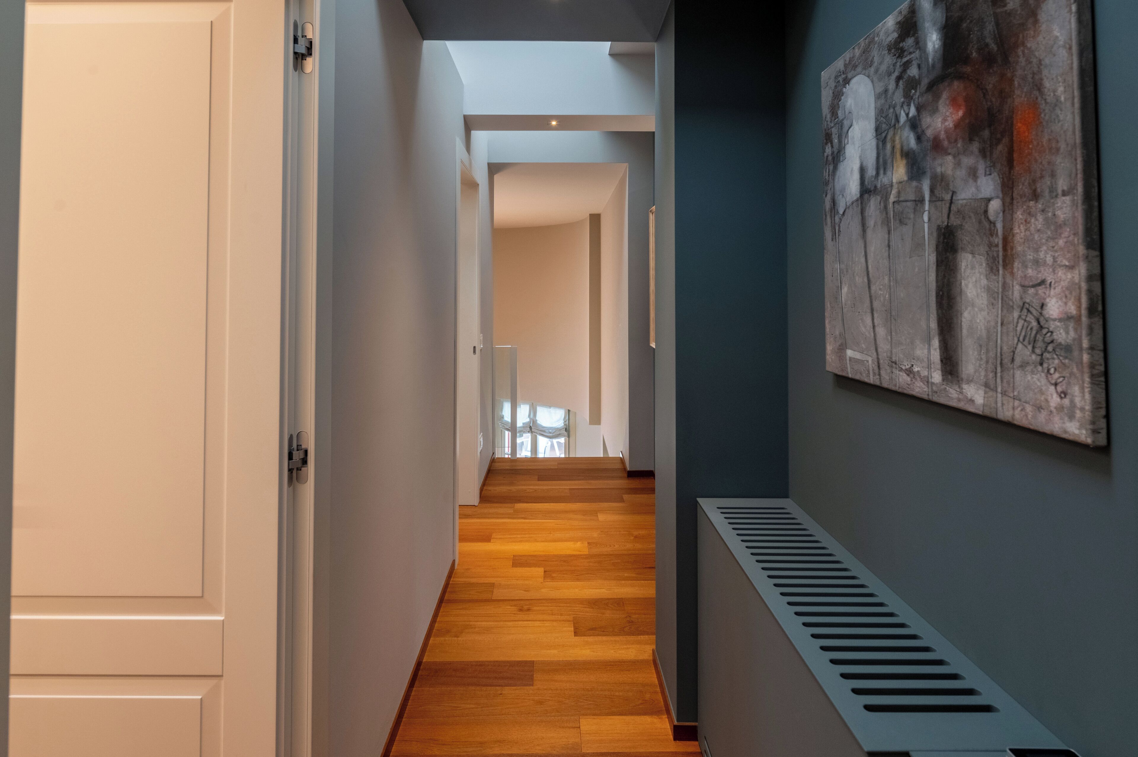 A hallway with wooden flooring, white walls, and a radiator.