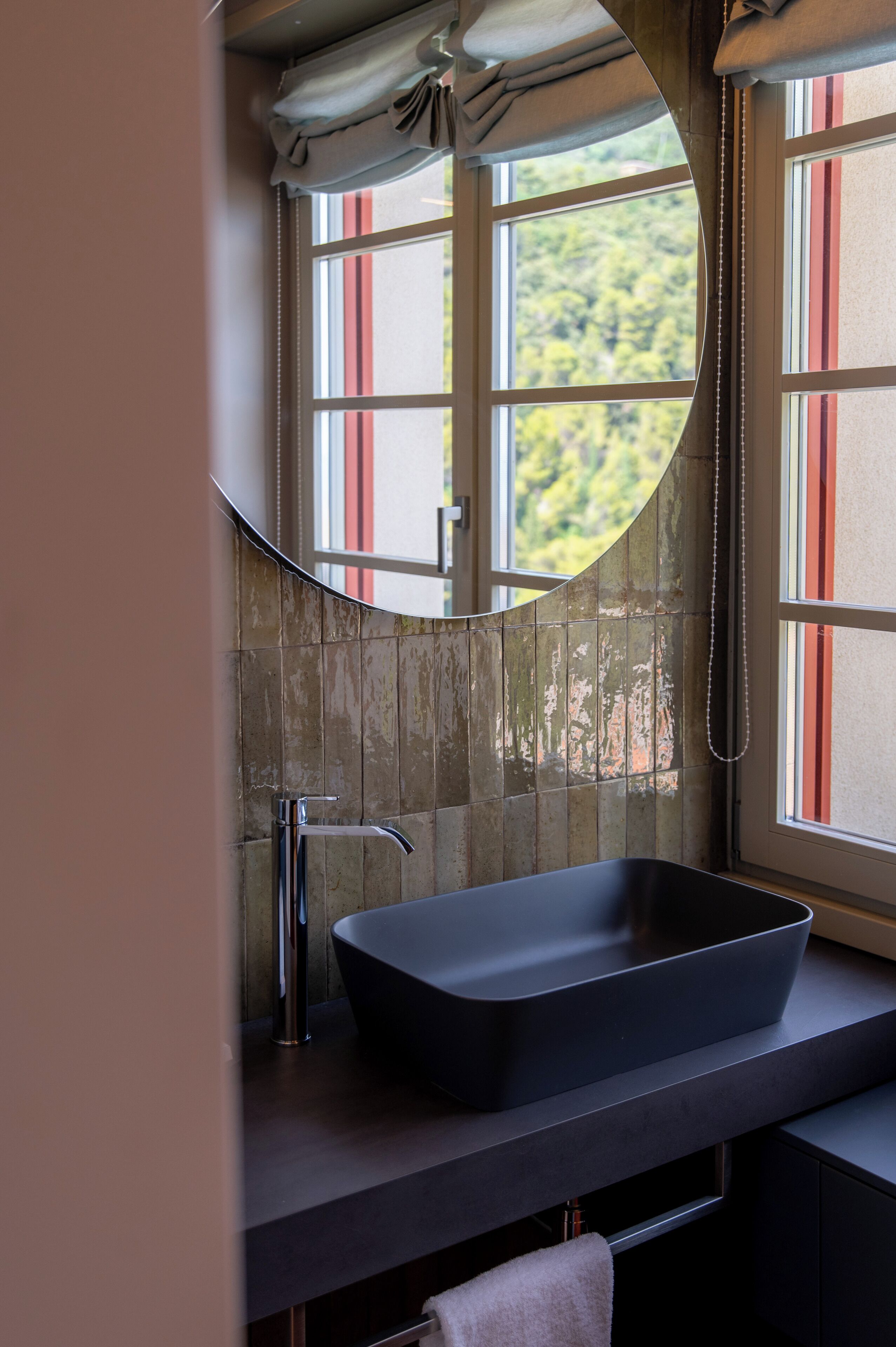 Un baño con un espejo grande, un lavabo negro y una ventana con persianas a rayas rojas y blancas.