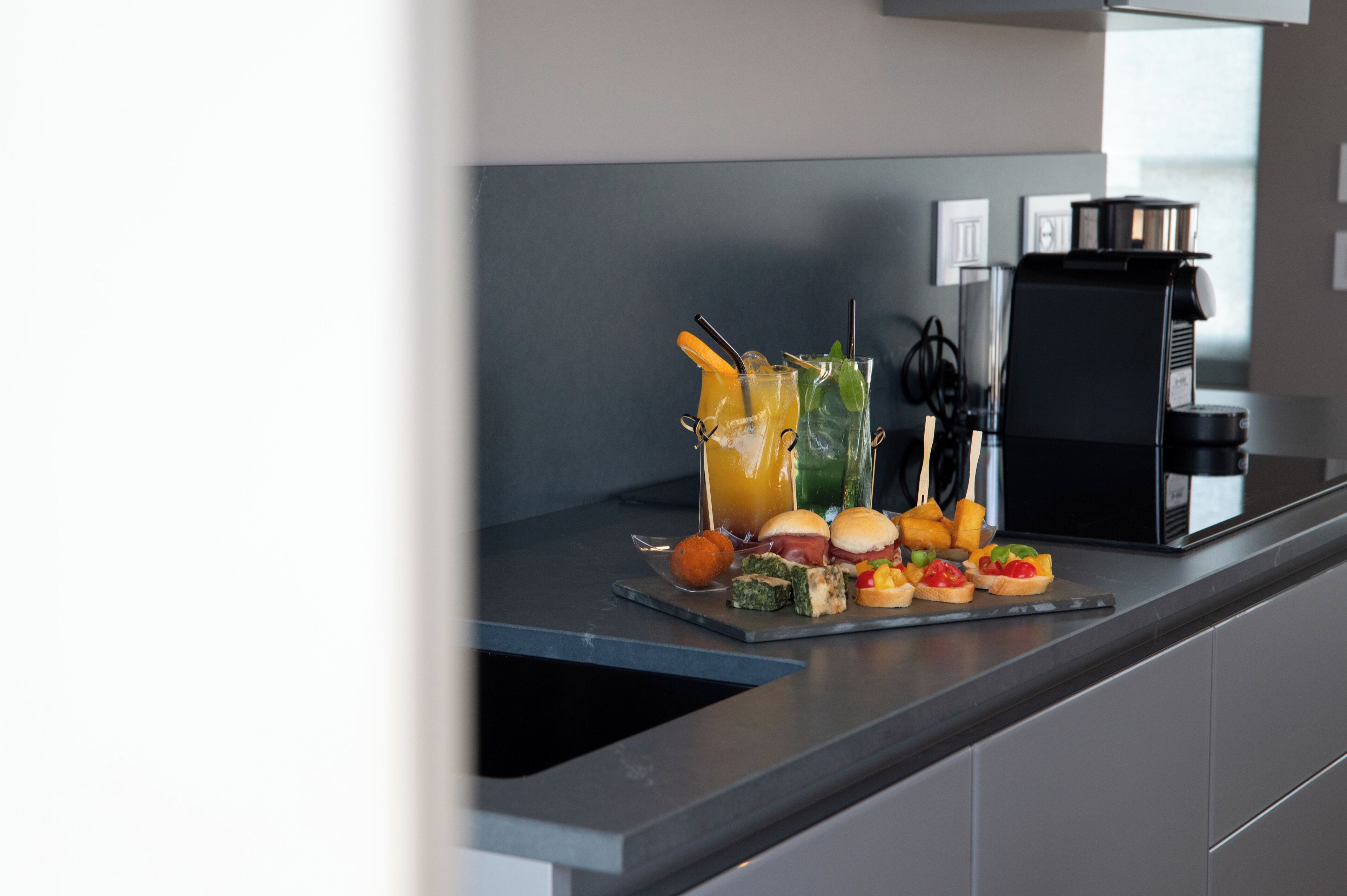 Una cocina moderna con una cafetera, un refresco de frutas y una variedad de aperitivos en la encimera.