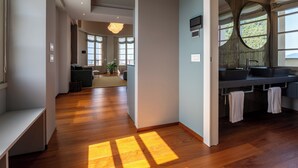 A modern hotel room with a wooden floor, a large window with a view, a built-in kitchen with a sink, and a seating area with a sofa and a coffee table. - Grand Hotel Torre Fara (Chiavari)