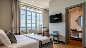 A hotel room with a large bed, a TV, a bathroom with a mirror, and a view of the sea. - Grand Hotel Torre Fara (Chiavari)
