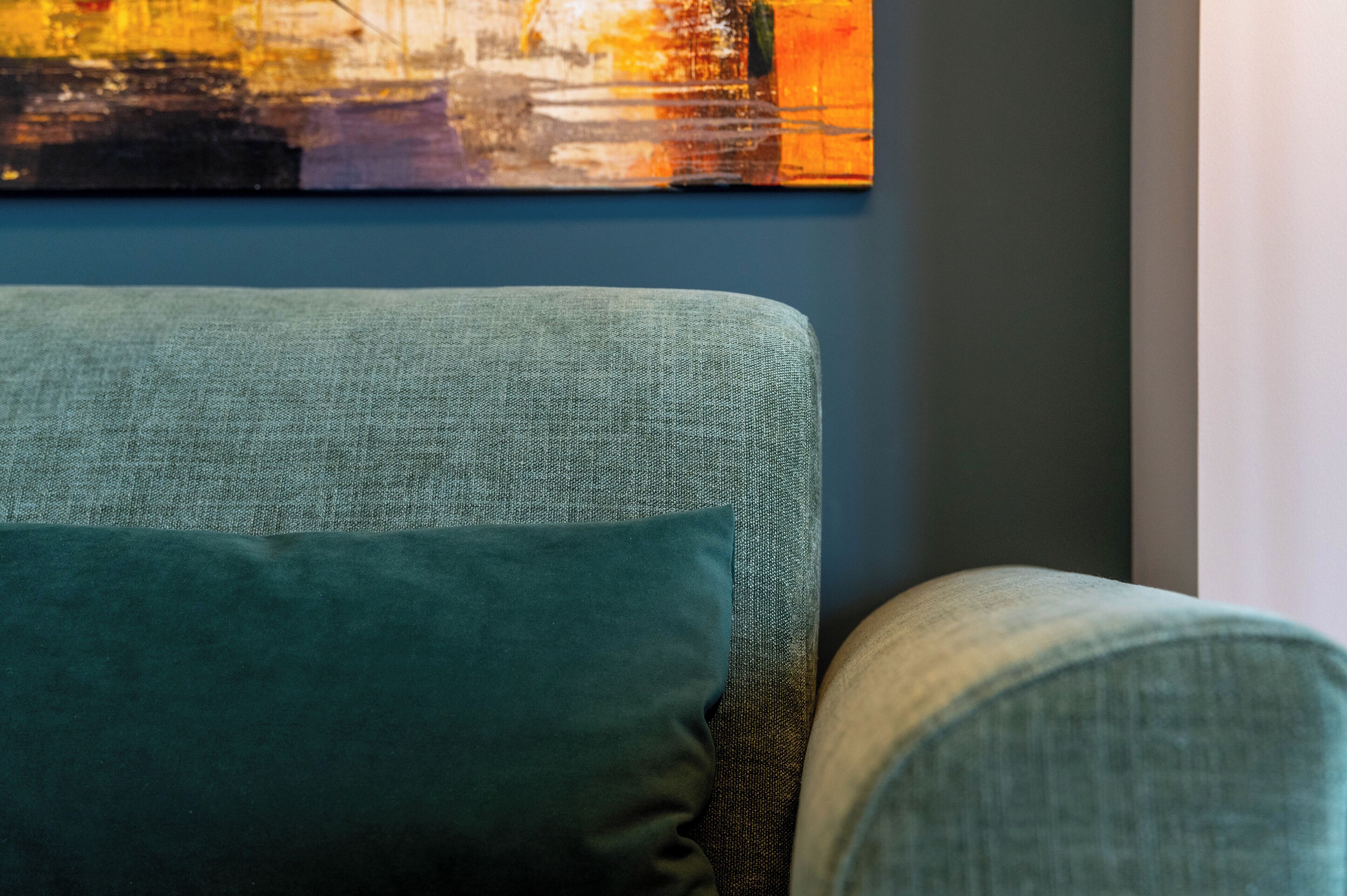 A room with a teal sofa and a painting on the wall.