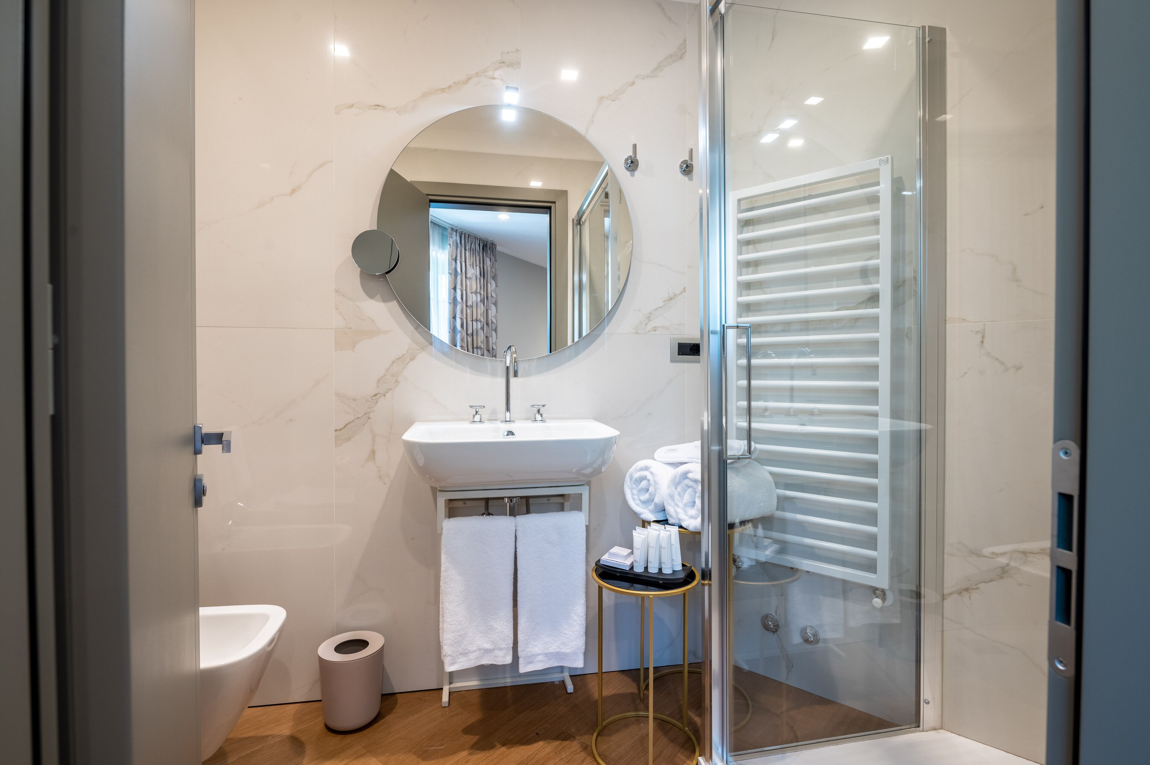 Un bagno moderno con box doccia in vetro, uno specchio rotondo, un lavandino e un porta asciugamani.