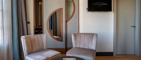 A hotel room with two armchairs, a small table, a TV on the wall, and a door.