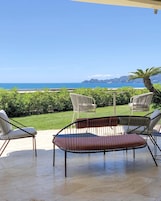 A patio with two chairs and a table, overlooking a scenic view of the sea and a distant mountain range.