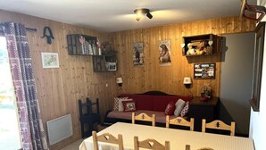 Una habitación acogedora con una pared de madera, una mesa de comedor con sillas, un sofá rojo y una pequeña estantería.