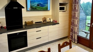 Una cocina moderna con horno integrado, una campana extractora negra y un televisor de pantalla plana sobre la encimera.