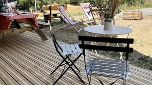 Una terraza de madera con una mesa, sillas, una planta en maceta y vistas a montañas.