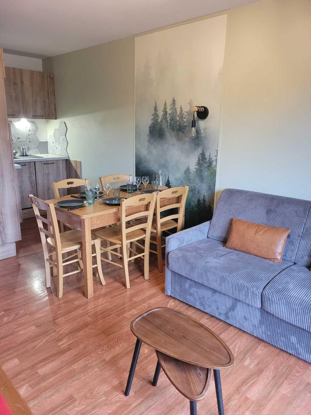 Uma sala de jantar com mesa e cadeiras de madeira, um sofá e uma parede com um mural de floresta.