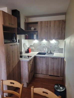 A compact kitchen with wooden cabinets, a microwave, a sink, and a hexagonal tile backsplash.