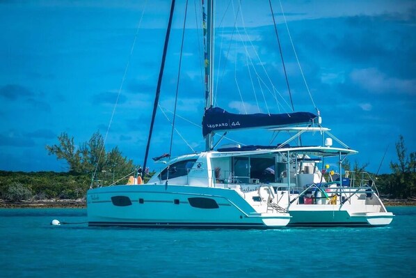 A white yacht with a covered deck and a mast, anchored in clear blue waters with a tropical landscape in the background. - Bahamas Luxury Sailing Catamaran, Nassau to Exumas (Staniel Cay)