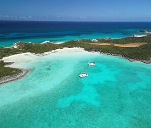 An aerial view of a turquoise lagoon with two boats anchored, surrounded by lush greenery and a sandy beach. - Bahamas Luxury Sailing Catamaran, Nassau to Exumas (Staniel Cay)