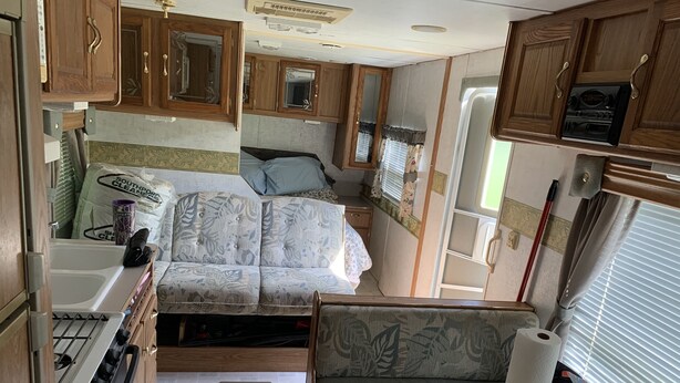 Interni di un camper compatto con angolo cottura, un letto e un piccolo spazio da pranzo.