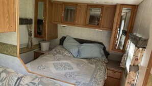 Camera a letto compatta in camper, con un letto, mobili in legno, un comodino e uno specchio.