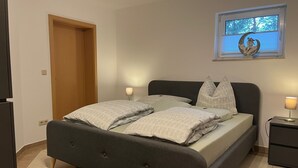 A bedroom with a bed, two bedside lamps, a window with a moon decoration, and a door. - Vacation apartment RhönPanorama EG (Kaltennordheim)