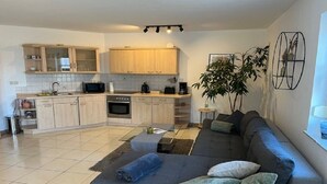 A modern kitchen with wooden cabinets, a microwave, and a coffee maker. There is a grey sofa with cushions and a small side table with a plant. - Vacation apartment RhönPanorama EG (Kaltennordheim)