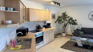 A compact kitchen with wooden cabinets, a built-in oven, and a sink. There's a dining area with a modern sofa and a coffee table. - Vacation apartment RhönPanorama EG (Kaltennordheim)