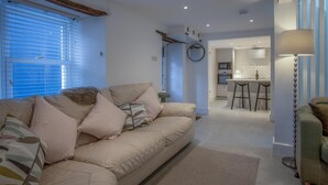 A modern living room with a beige sofa, a coffee table, and a dining area with a kitchen in the background. - Caleb's Cottage - 4 Bedroom Cottage - Solva (Haverfordwest)