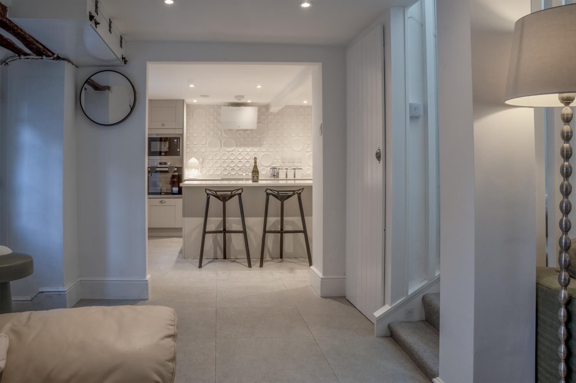 Una cocina moderna con una isla central, dos taburetes de bar y un comedor con techo alto e iluminación empotrada.