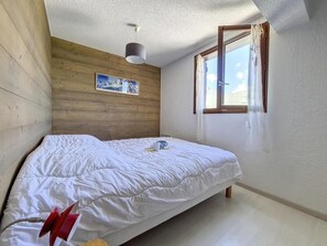 A bedroom with a wooden wall, a bed with white bedding, a window with curtains, and a ceiling light. - 200m from resort center, 1st floor, view mountain, balcony, tv, ski locker, 66m² (Saint-Martin-de-Belleville)