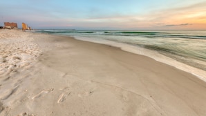 A beach with a pier extending into the ocean, sandy shore, and buildings in the background.