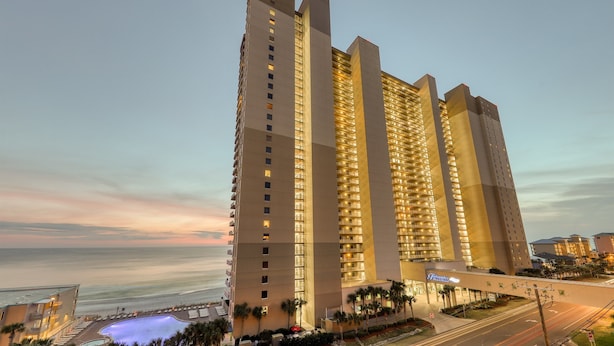 A high-rise hotel with multiple floors, a swimming pool, and a view of the ocean.