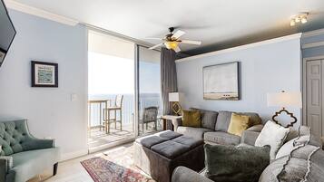 A living room with a sofa, ottoman, and a chair, a ceiling fan, and a view to the outside.