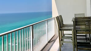 A balcony with a view of the ocean, wooden chairs, and a white railing.