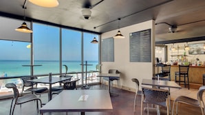 A restaurant with a view of the ocean, featuring tables and chairs, a bar area, and menu boards.