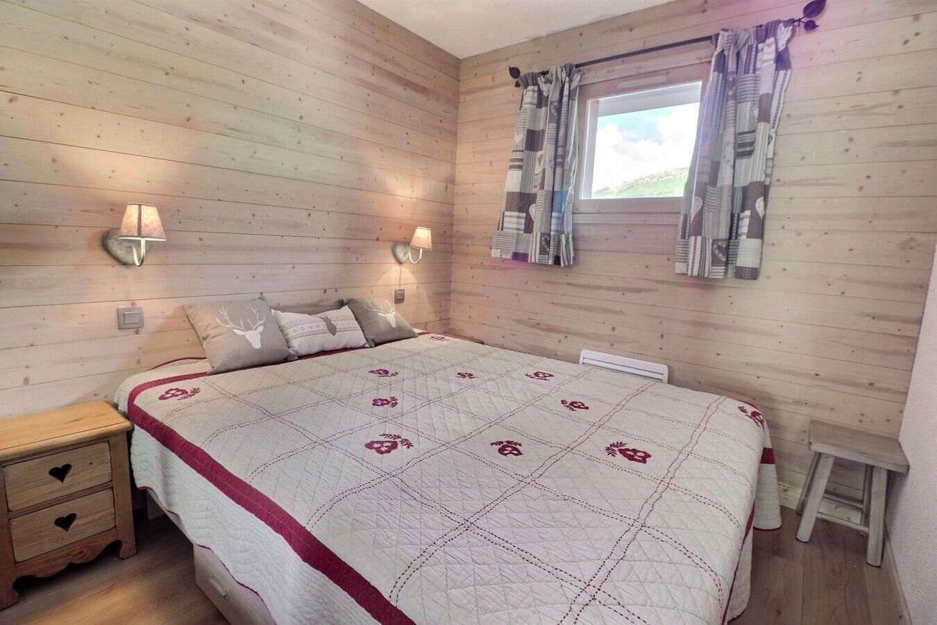 Een kamer met houten lambrisering, een bed, nachtkastjes en een raam met gordijnen.