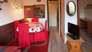 Een knus ingerichte kamer met een eettafel gedekt voor twee personen, een televisie op een houten standaard en een spiegel aan de muur.