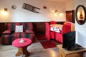 A living area with a sofa, a dining table, and a television on a wooden stand.