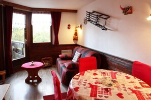 A cozy room with a sofa, a table with a patterned tablecloth, and a window with curtains.
