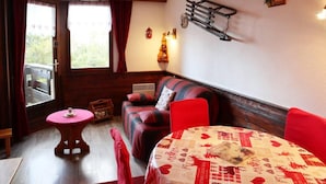 Een gezellige kamer met een houten bank, een rode bank, een tafel met een gedessineerd tafelkleed en een raam met gordijnen.