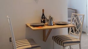 A dining area with a wooden table, two striped chairs, a decorative wall piece, and a bottle of wine. - Grand Panoramic Villa Ozar (Mykonos)