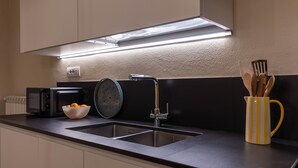 Uma cozinha moderna com bancada preta, pia de aço inoxidável e uma caneca listrada de amarelo.