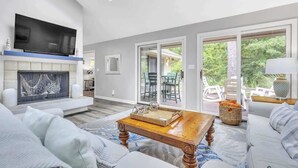 A modern living room with a fireplace, a flat-screen TV, and a large window overlooking a patio area. - Stylish Sea Pines Home Hot Tub, Hilton Head (Hilton Head Island)